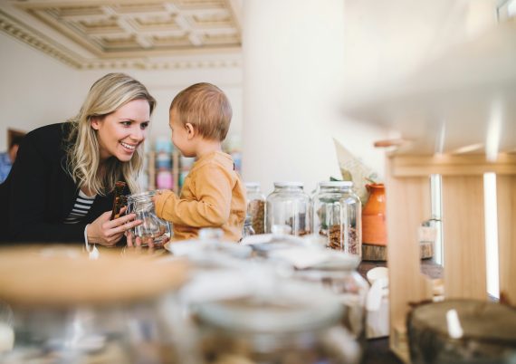 A young woman with a toddler boy buying groceries in zero waste shop.