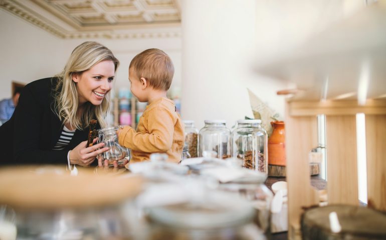 A young woman with a toddler boy buying groceries in zero waste shop.