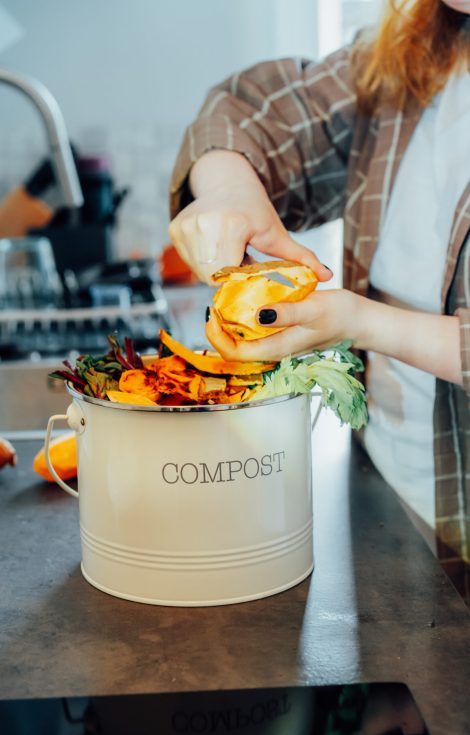 Compost the kitchen waste, recycling at home. Compost bin with vegetables cutted leftovers on the kitchen table with blurred woman cooking meal. Environmentally responsible, ecology. Selective focus.