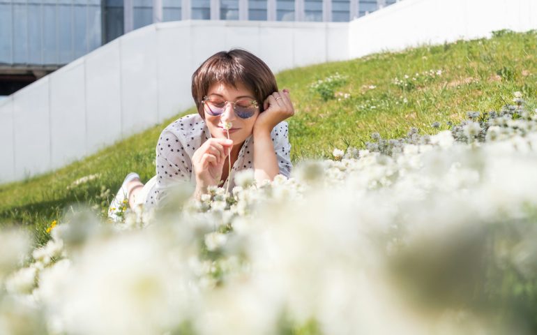 Woman in colorful sunglasses relaxes on lawn in urban park. Summer vibes. Nature in town.